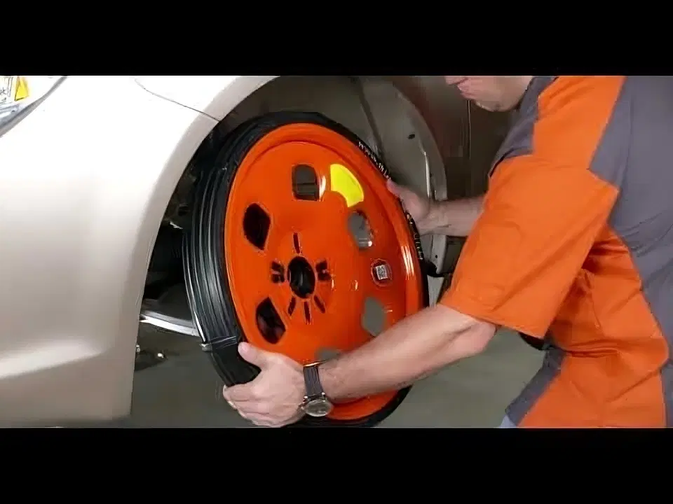 Workshop mechanic fitting orange GuniWheel universal temporary wheel onto a silver vehicle